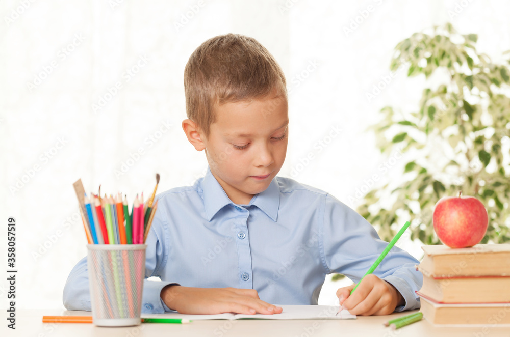 Young schoolboy sitting at the table and doing homework Young schoolboy sitting at the table and doing homework