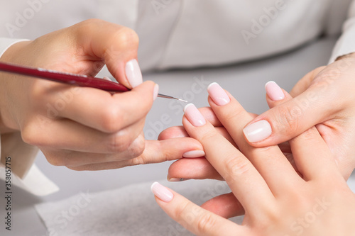 Stampa su tela Hand of young woman receiving french manicure by beautician at nail salon