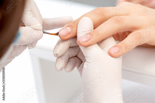 Close up of hand of manicurist applying clear nail polish in beauty salon.