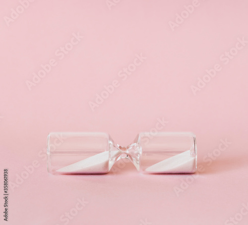 Hourglass on pink and white background, sand flowing through the bulb of sandglass measuring time. minimal concept.