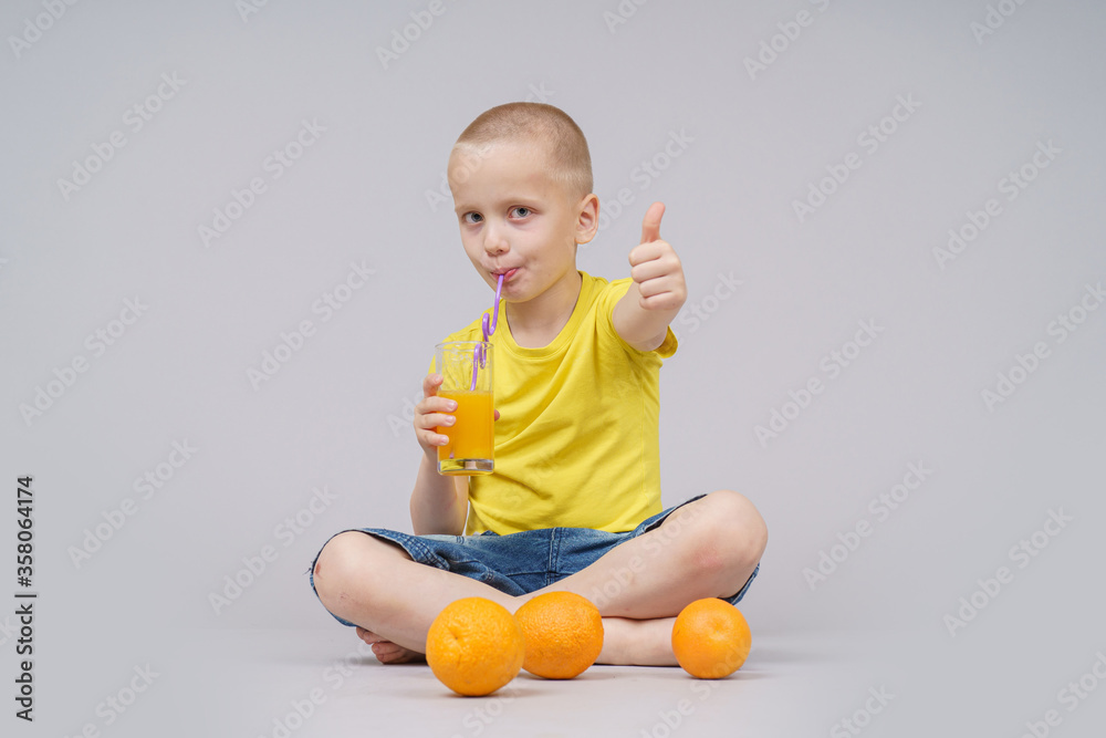 Smiling boy sitting with fruit orange and drink. Isolated on gray Smiling boy sitting with fruit orange and drink. Isolated on gray