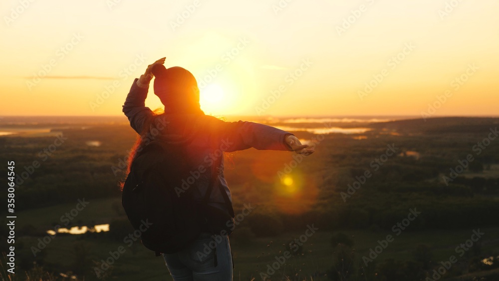 free girl tourist travels in nature alone. A young woman traveler with a backpack comes to edge of peak of sunrise, raises her hands in air and spins, enjoys victory, beautiful dawn and landscape.