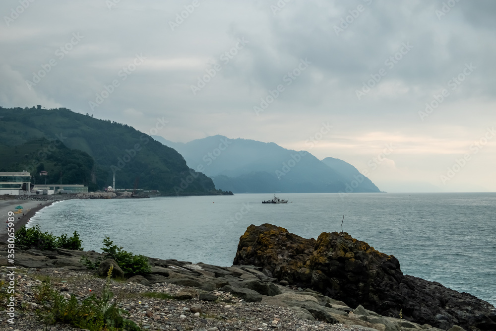 Landscape with mountains. Panoramic view with hills and sea. Pebble beach. Stones, boulders on the shore, green vegetation on the mountains. Day. Mainly cloudy. Georgia.