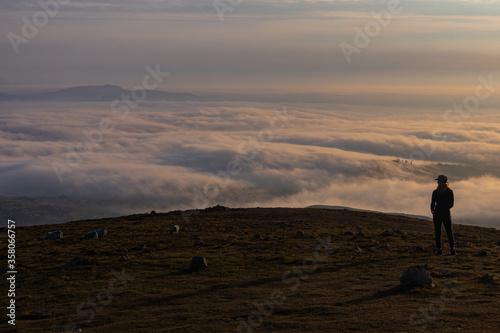 Early morning mountain top cloud inversion with young hiker silhouetted enjoying the view, Slieve Meelmore, Mourne Mountains, County Down, Northern Ireland, Area of Outstanding Natural Beauty