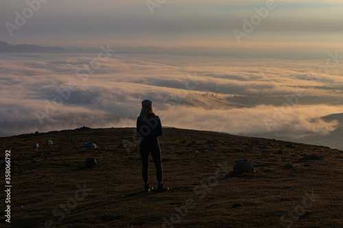 Early morning mountain top cloud inversion with young hiker silhouetted enjoying the view, Slieve Meelmore, Mourne Mountains, County Down, Northern Ireland, Area of Outstanding Natural Beauty