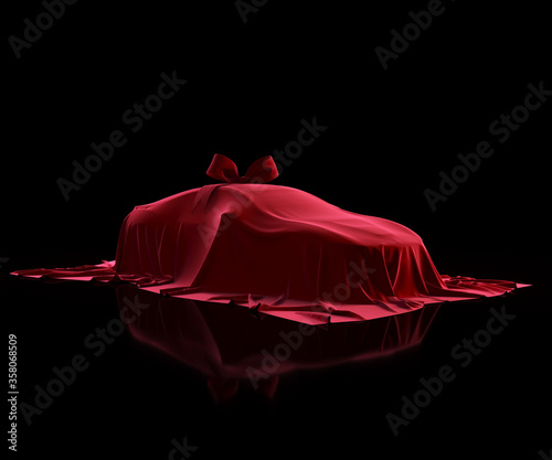 Car covered by red velvet fabric with gift bow-knot on a black background. Vehicle veiled by red cloth. Luxury prize, gift.
