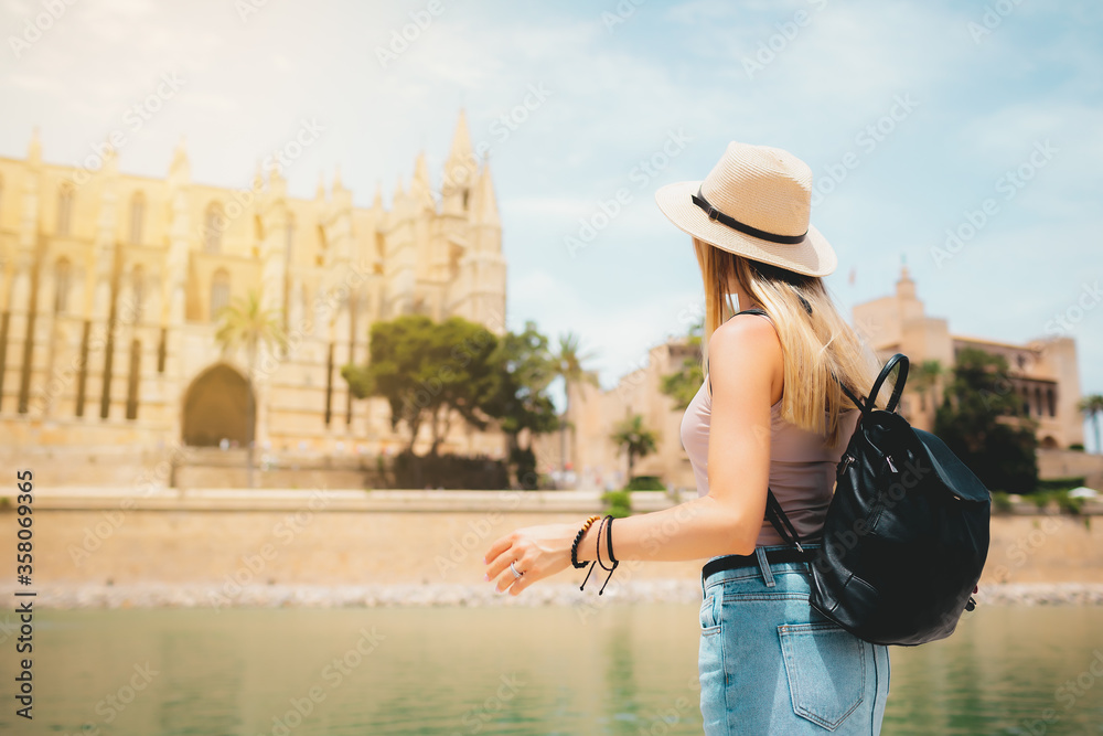 Summer hot vacation Europe Spain Mallorca Palma holiday travel tourism architecture - young beautiful Caucasian walking attractive young girl with hat and backpack in front of the city castle