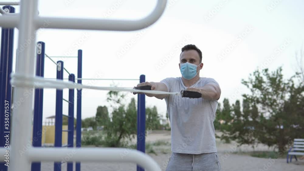 During the quarantine period, the athlete plays sports on the street in a mask. Athlete does exercises with an expander. During the quarantine period, the athlete plays sports on the street in a mask. Athlete does exercises with an expander.