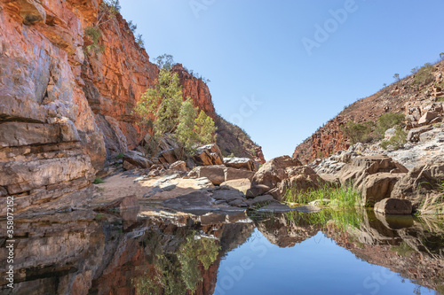 Still water pound. Orange rock walls reflected on the water. Still and calm water. No people. No clouds. Clean landscape. Ormiston gorge, Macdonnell ranges, Northern Territory NT, Australia, Oceania © Alba