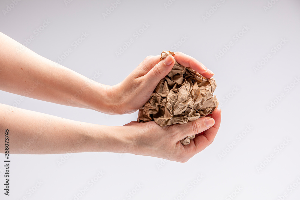 Close-up of a white people's hand crushing a crumpled piece of brown paper in front of a white background Close-up of a white people's hand crushing a crumpled piece of brown paper in front of a white background