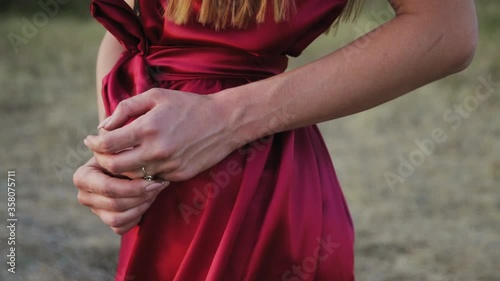 Girl in a burgundy dress with a long wedding ring on her finger at sunset.  photo