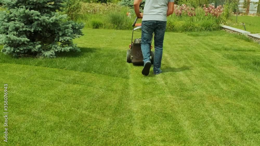 Lawn mower cutting the grass. Gardening activity. Cutting grass with petrol driven lawn mower in sunny garden. Gardener working with mower machine in the garden. Lawn mower cutting green grass Lawn mower cutting the grass. Gardening activity. Cutting grass with petrol driven lawn mower in sunny garden. Gardener working with mower machine in the garden. Lawn mower cutting green grass