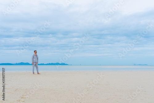 a man walks along the beach in seclusion from everyone, keeping a safe distance, a yellow backpack with a painted smile, a person in a gray tracksuit on the beach in Thailand, freedom from everyone