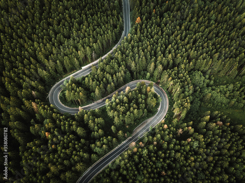 Aerial view of countryside road passing through the green forest and mountain