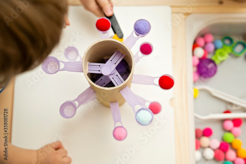 Make it at home. DIY toy for improvement of coordination, balance and fine motor skills. Kid inserting pompons into dosing teaspoons.