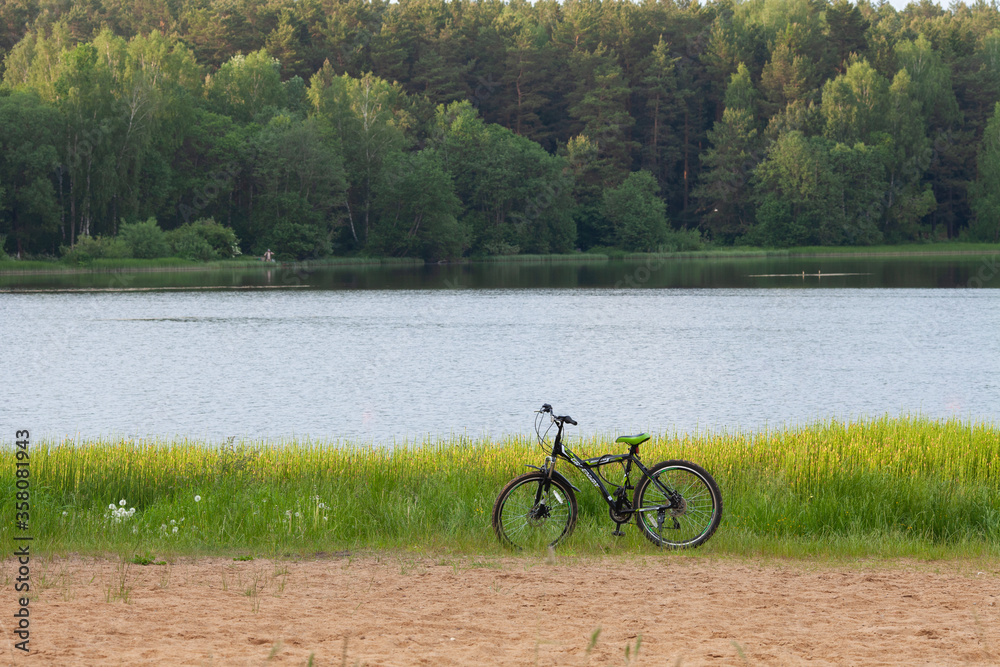 A bicycle parked on a sand beach at a shore lake in summer. Beautiful natural landscape. Active lifestyle and sport activities in quarantine and social isolation conditions.