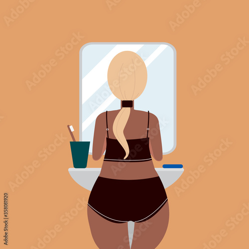 A tanned, plump girl with long hair tied in a ponytail looks in the bathroom mirror. A woman loves her body. Body positive.