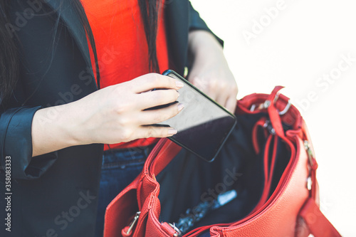 A hand put the phone in the female red leather handbag