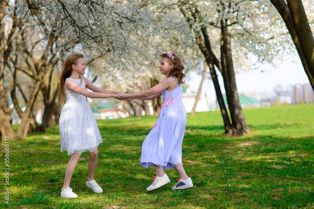Beautiful young girls with blue eyes in a white dresses in the garden with apple trees blosoming having fun and enjoying smell of flowering spring garden. Beautiful young girls with blue eyes in a white dresses in the garden with apple trees blosoming having fun and enjoying smell of flowering spring garden.