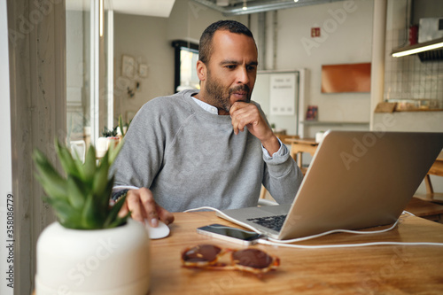 Photos Casual businessman intently working on laptop in cafe