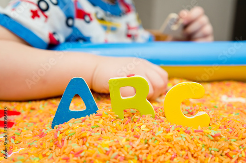 Kid learning ABC's. Early education for toddlers with colored rice as sensorial elements. Therapy for children with easy learning.