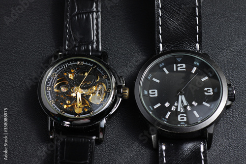 a black automatic self winding wristwatch with transparent sekeleton dial design and a black battery operated watch on black leather background photo