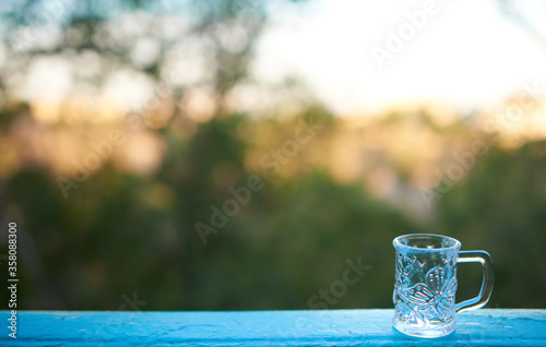 An empty glass cup stands on the railing of the balcony against the backdrop of a summer evening. Copy space