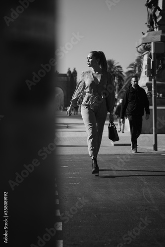 Young attractive stylish woman walking along busy city street. Black and white