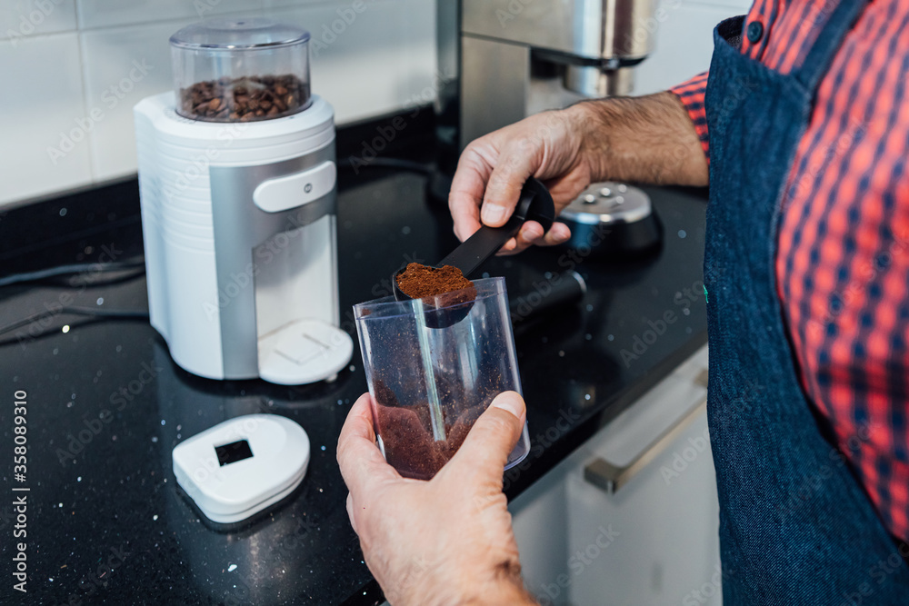 Man wearing plaid shirt and apron throws the ground coffee into the coffee pot