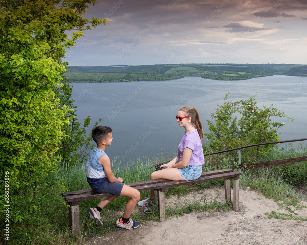 Fototapeta premium Sister and brother sitting on bench at pond