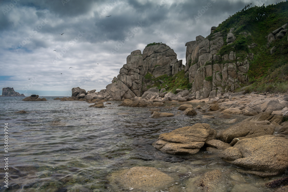 Naklejka premium Sea shore with large stones on a background of cloudy sky and flying gulls