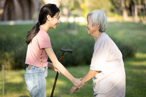 Asian granddaughter is giving a walking stick to her old grandmother,persuade her senior woman to take a walk,exercise in the garden together,happy child girl visiting the elderly at nursing home © Satjawat