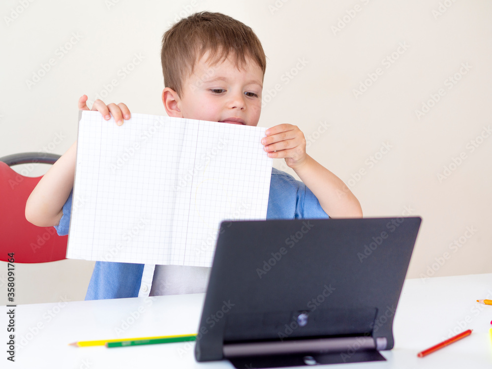 Online learning for children. A child shows his homework to the tablet camera. Writing school tasks while homeschooling, while school closed due to Coronavirus Online learning for children. A child shows his homework to the tablet camera. Writing school tasks while homeschooling, while school closed due to Coronavirus