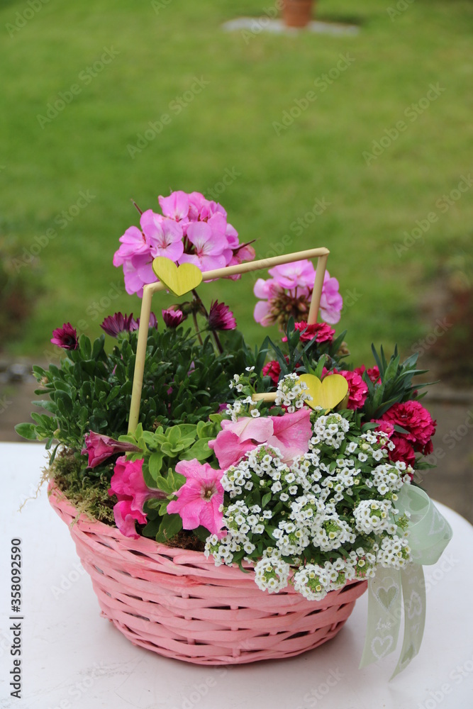 Körbchen mit Blumen und Herz als Geschenk im Garten
