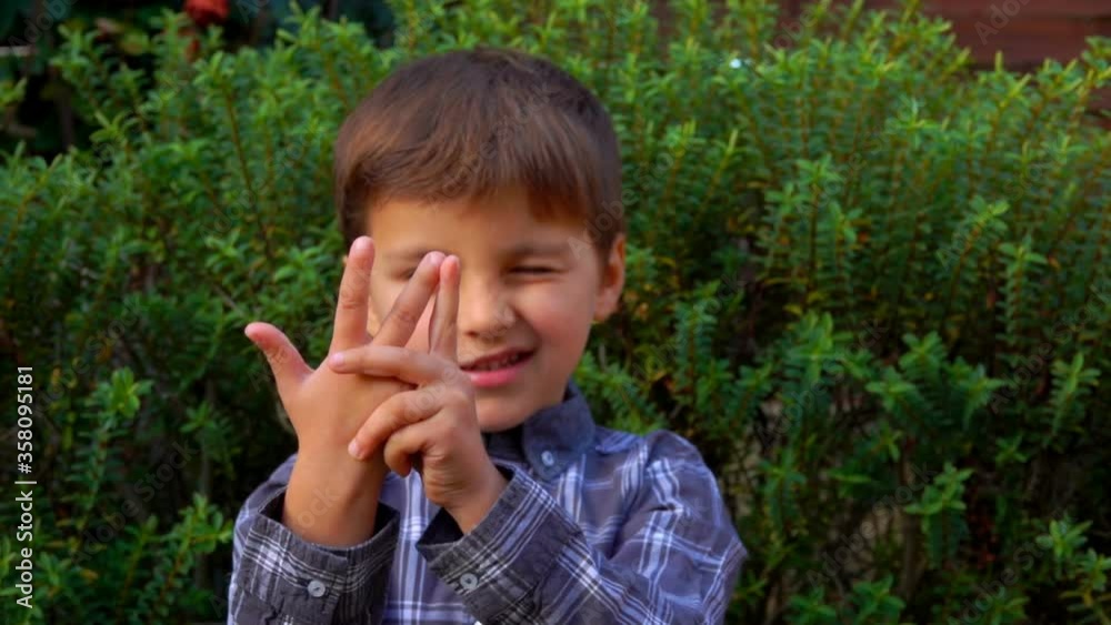 Adorable boy is counting on fingers outdoors on the background of green bush Adorable boy is counting on fingers outdoors on the background of green bush