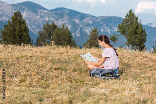 Hiker girl looking at a map sitting on the meadow in a beautiful place © nacho roca