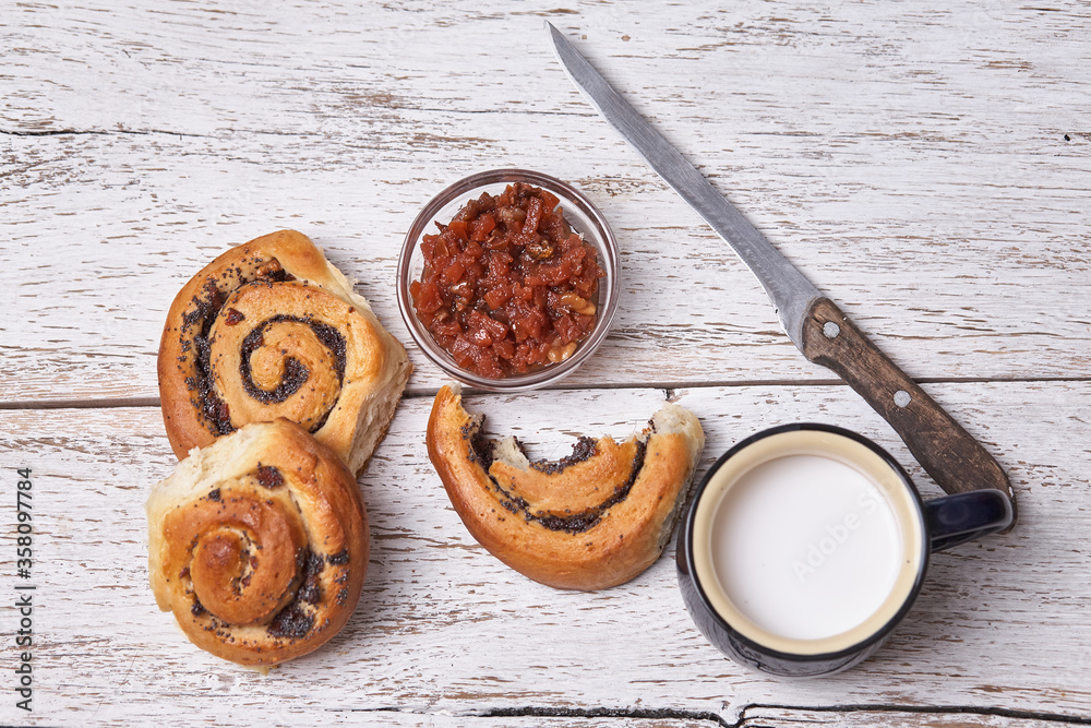 Variety of homemade puff pastry buns cinnamon served with milk cup, jam, butter as breakfast over white plank wooden background. Flat lay, space