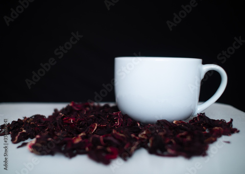 White Wooden Table with a Mug and Hibiscus Flower / Roselle (Hibiscus Sabdariffa) in a Black Background