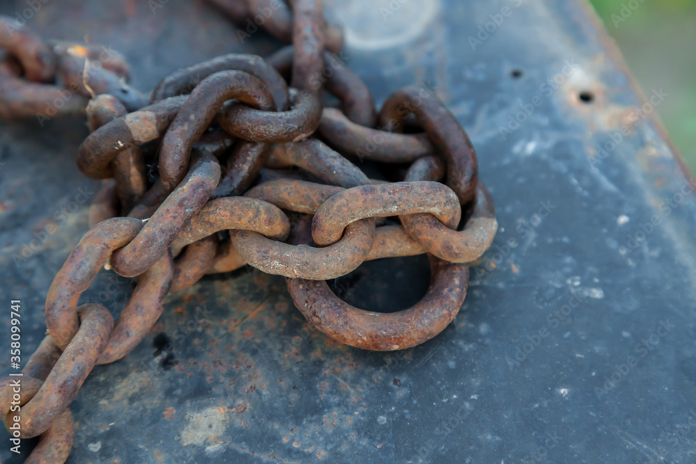 Forged old metal chain on the pier moored boat with peeling blue paint from the water, iron covered with rust. Forged old metal chain on the pier moored boat with peeling blue paint from the water, iron covered with rust.