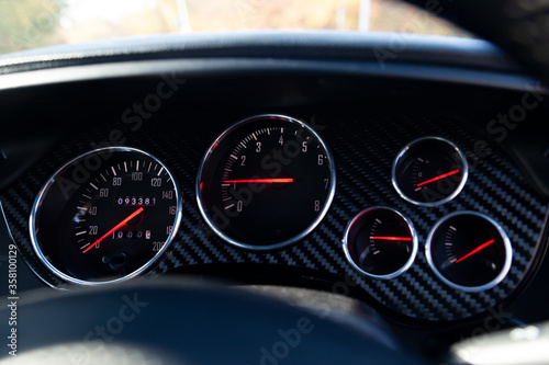 Stylish backlit dashboard with sensors for measuring speed, engine temperature and pressure against a blue and black chess designer’s design drawing in the car’s interior.