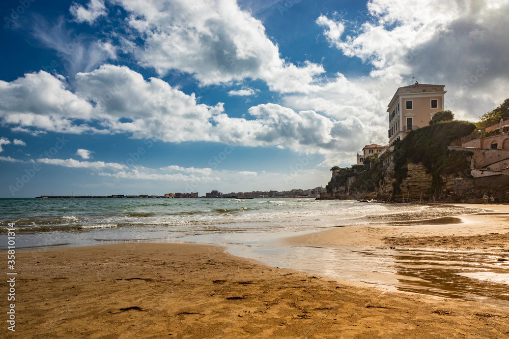 The houses and palaces of the city of Nettuno, on the cliff overlooking the sea. Cloudy blue sky, the wind, the waves of the rough sea. The Roman coast, Lazio, Italy.