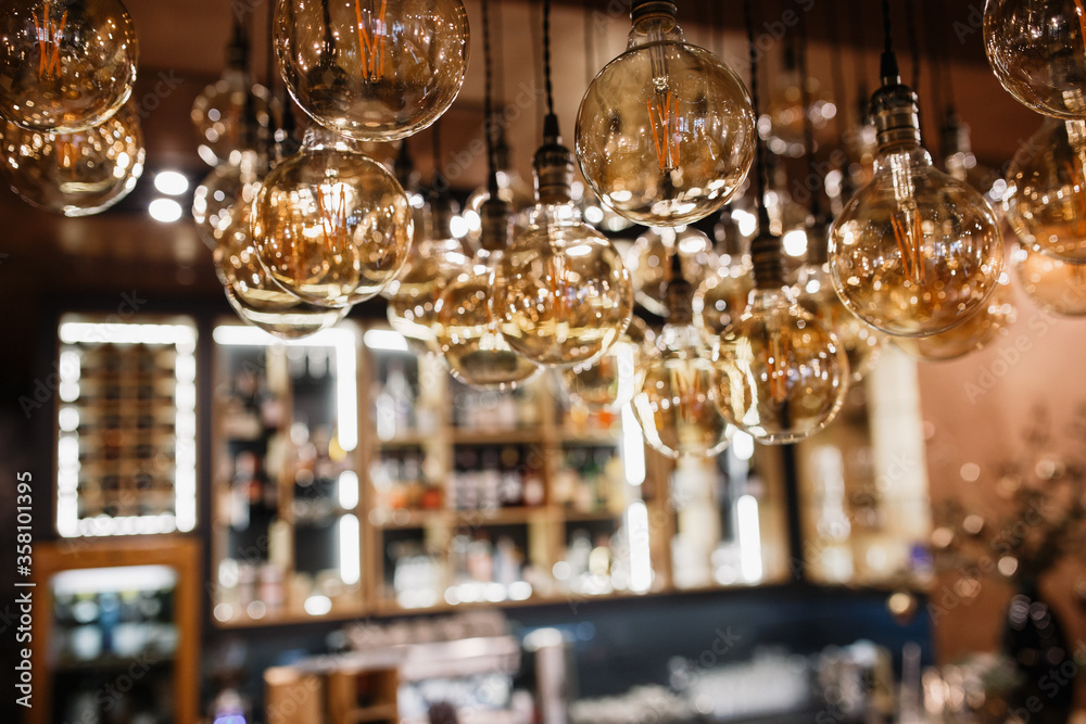 Round light bulbs in the foreground. Bar counter with alcohol in the background in blur. Glass bottles on the shelves. Round light bulbs in the foreground. Bar counter with alcohol in the background in blur. Glass bottles on the shelves.
