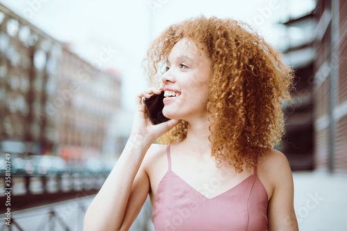 Primer plano de una hermosa modelo joven   hablando por teléfono celular en plena calle. Retrato cercano de una bella chica brasileña con un gesto cotidiano como hablar por teléfono en plena calle. 