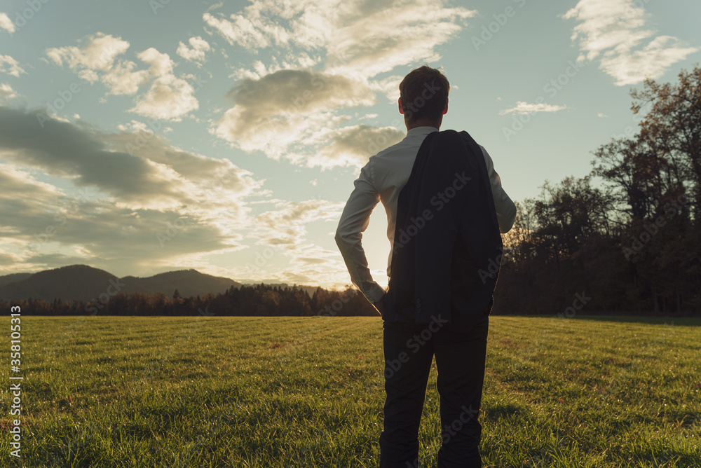Young businessman standing in autumn meadow gazing into the future - obrazy, fototapety, plakaty 
