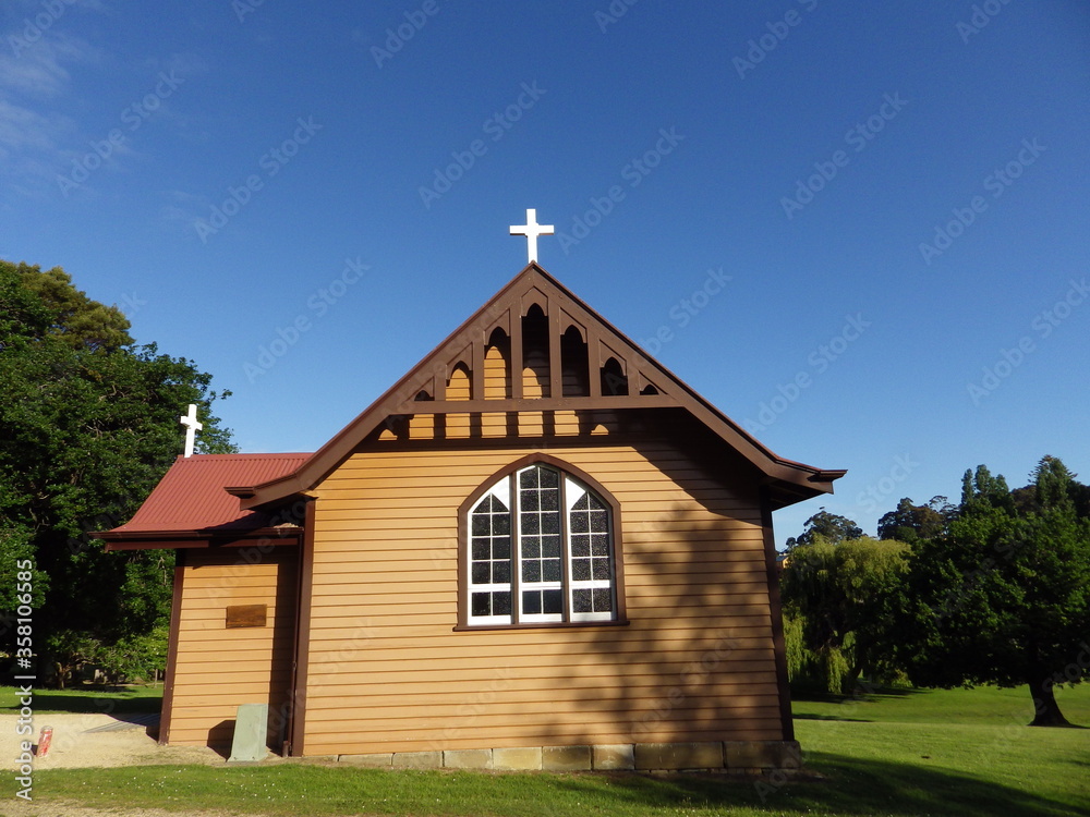 beautiful small church on the green meadow and blue sky  with white cross brown wooden wall and red roof port arthur tasmania australia