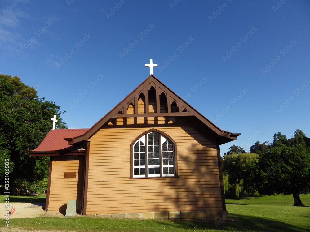 beautiful small church on the green meadow and blue sky with white cross brown wooden wall and red roof port arthur tasmania australia beautiful small church on the green meadow and blue sky with white cross brown wooden wall and red roof port arthur tasmania australia