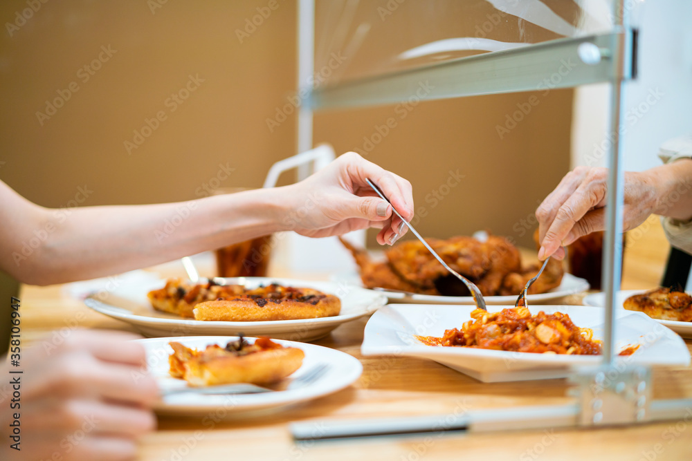 Asian woman eating food while siting separate and keep distance with table plastic shield partition in restaurant, new normal, restaurant, coronavirus outbreak and social distancing concept