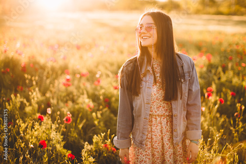 Cheerful young woman in casual jeans dress walking through beautiful flower filed at golden sunrise in summer. Young woman enjoying flower, nice female lying down in meadow. Harmony concept