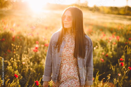 Cheerful young woman in casual jeans dress walking through beautiful flower filed at golden sunrise in summer. Young woman enjoying flower, nice female lying down in meadow. Harmony concept