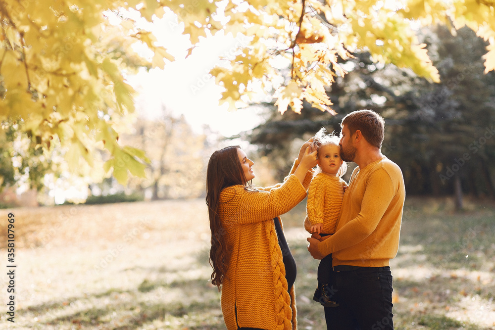 Naklejka premium Family in a autumn park. Woman in a yellow sweater. Cute little girl with parents